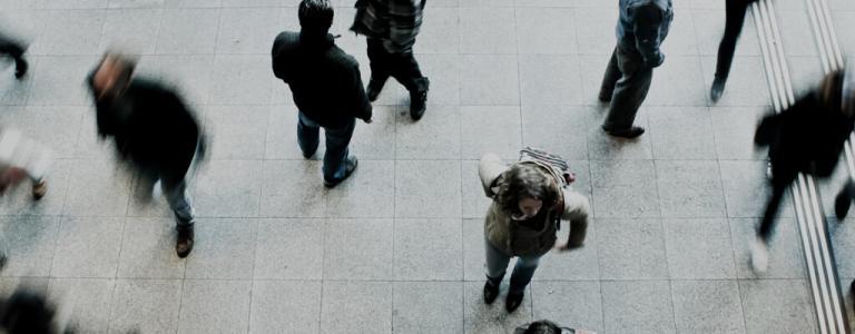 Sicht von oben auf Menschen, die zu Fuß auf einem offenen Platz unterwegs sind.